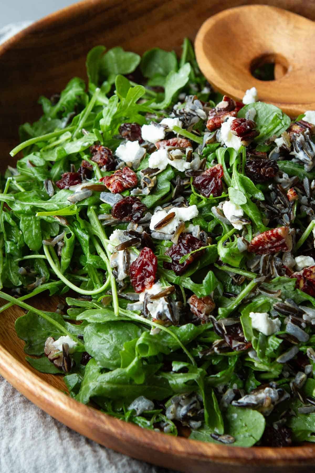 A wooden bowl filled with wild rice arugula salad.