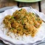 Chicken curry with potatoes and rice on a white plate.