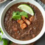 Black bean soup with hame and a lime wedge in a bowl.
