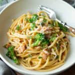 Bucatini noodles with salmon, broccoli and dill in a white bowl.