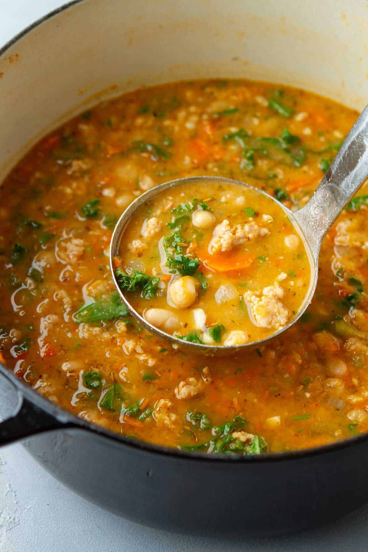A saucepan filled with sausage, bean and kale soup.